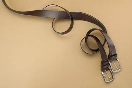 Two leather belts on beige background, flat lay. Space for text