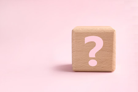 Wooden cube with question mark on pink background, closeup. Space for textの写真素材
