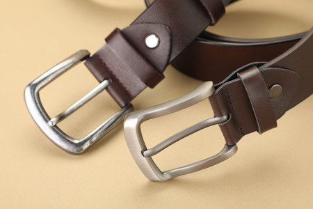 Two leather belts on beige background, closeup