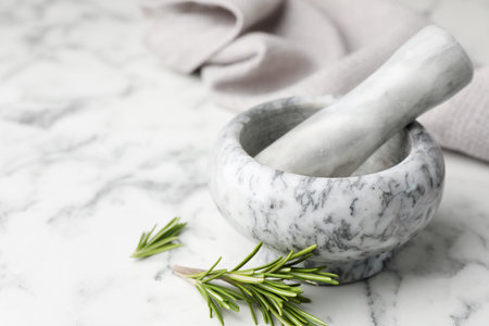 Mortar with rosemary, pestle and cloth on white marble table, closeup. Space for textの写真素材