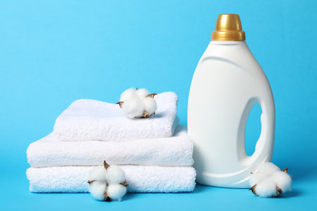 Bottle of fabric softener, cotton flowers and towels on light blue backgroundの写真素材