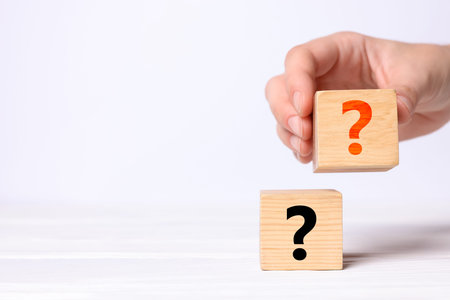 Woman holding cube with question mark at white table, closeup. Space for text