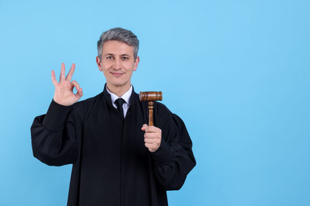 Judge with mallet showing ok gesture on light blue background. Space for textの写真素材