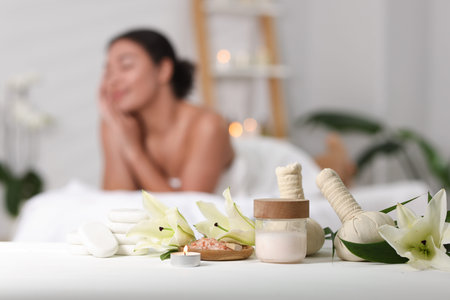 Beautiful woman relaxing on massage couch indoors, focus on different spa products and lily flowers