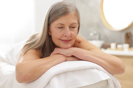 Senior woman relaxing on massage couch in spa salonの写真素材