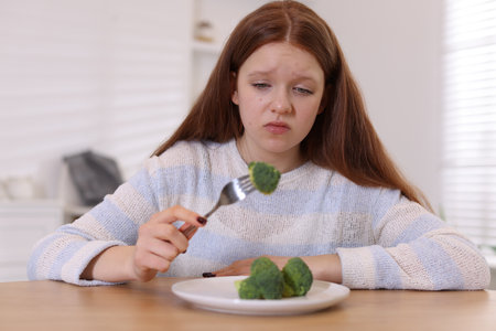 Sad teenage girl with broccoli at wooden table. Eating disorderの写真素材