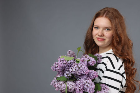 Beautiful teenage girl with bouquet of lilac flowers on grey background. Space for textの写真素材