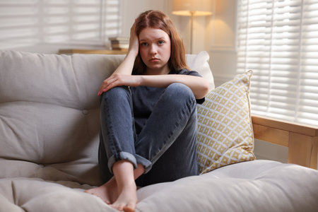 Sad teenage girl on sofa at homeの写真素材