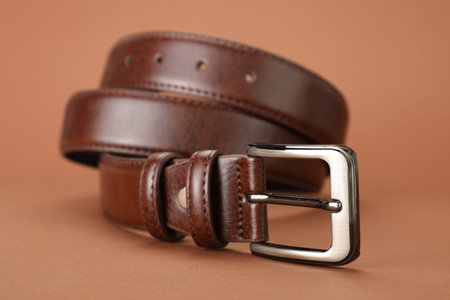 One leather belt on pale brown background, closeup