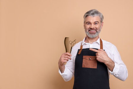 Smiling hairdresser with scissors and comb on beige background, space for textの写真素材