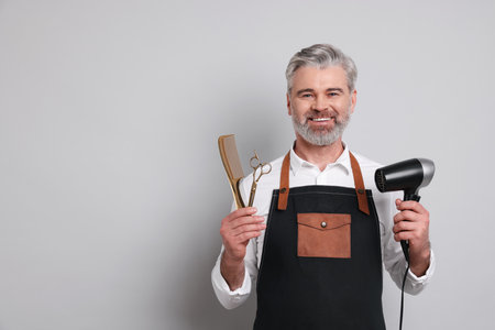 Smiling hairdresser with dryer, scissors and comb on gray background, space for textの写真素材