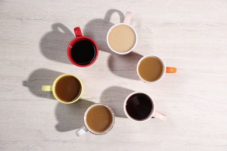 Different cups with aromatic coffee drinks on light wooden table, flat layの写真素材