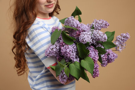 Teenage girl with bouquet of lilac flowers on beige background, closeupの写真素材