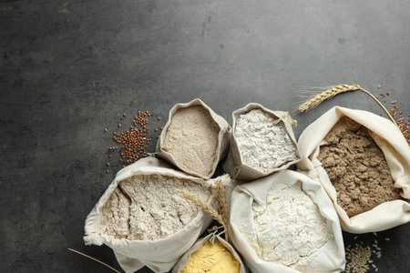 Different types of flour in bags on gray table, flat lay. Space for text