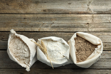 Different types of flour in bags on wooden table, flat lay. Space for textの写真素材