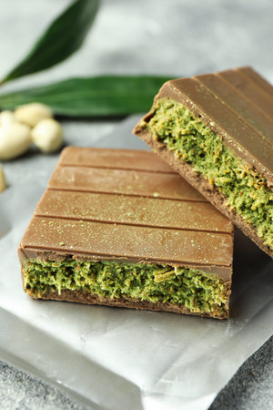 Pieces of tasty chocolate with pistachios and knafeh on grey textured table, closeup