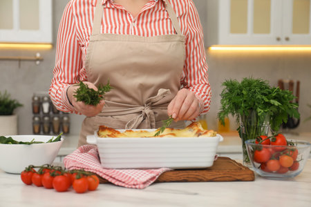 Woman putting rosemary onto lasagna at white marble table in kitchen, closeupのeditorial素材
