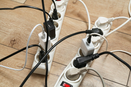 Extension power boards overloaded with plugs on wooden floor, closeup