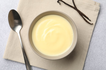 Tasty vanilla pudding in bowl, pods and spoon on light grey table, flat layの写真素材