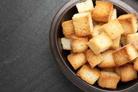 Tasty crispy croutons in bowl on dark textured table, top view. Space for textの写真素材