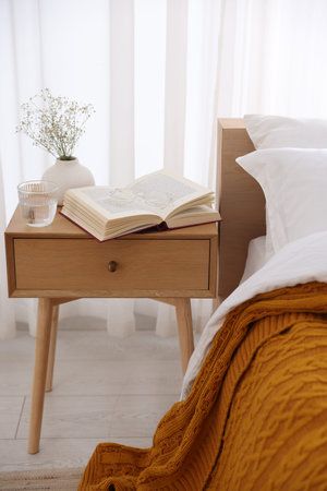 Bedside table with book, flowers in vase, glass of water and glasses near bed indoorsの写真素材