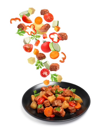 Delicious cooked stew. Fresh ingredients falling onto plate on white backgroundの写真素材