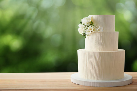 Beautiful wedding cake with floral decor on wooden table outdoors. Space for textの写真素材