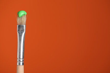 Brush with green paint on orange background, closeup. Space for textの写真素材