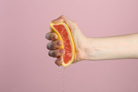Woman squeezing grapefruit on pink background, closeupの写真素材