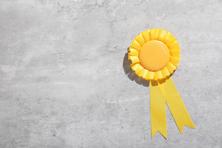 Yellow award ribbon on light gray table, top view. Space for text