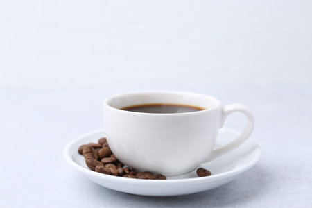 Aromatic coffee in cup, beans and saucer on light table, closeupの写真素材