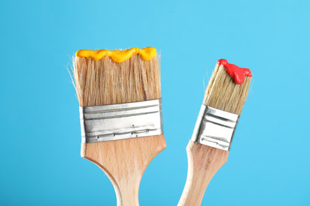 Two brushes with color paints on light blue background, closeupの写真素材