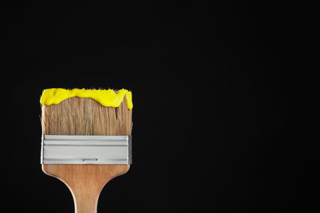 Brush with yellow paint on black background, closeup. Space for textの写真素材