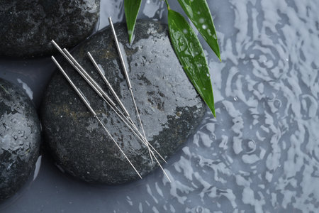 Acupuncture needles, spa stones and leaves in rippled water on grey background, top view. Space for textの写真素材