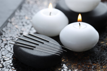 Acupuncture needles, spa stone and burning candles on dark textured background, closeupの写真素材