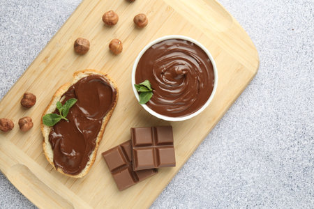 Tasty chocolate spread, toast, hazelnuts and mint on grey textured table, top view