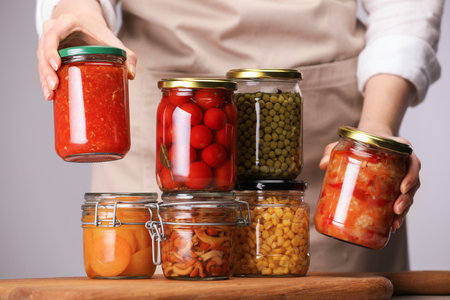Woman with jars of different pickled products at table against light gray background, closeupの写真素材