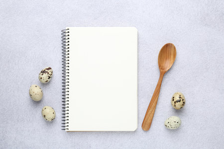 Blank recipe book, spoon and quail eggs on light table, top view. Mockup for designの写真素材