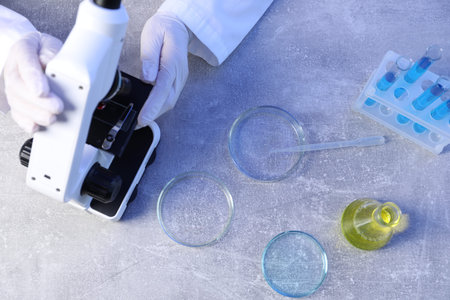 Scientist working with microscope and Petri dishes at table, top view
