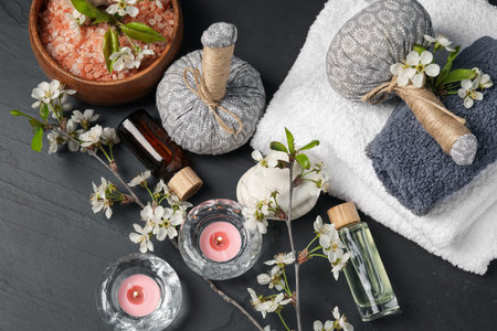 Spa composition with cosmetic products, burning candles and beautiful flowers on black textured...