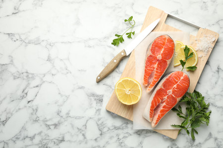 Seafood. Fresh raw salmon steaks, parsley, pieces of lemon and salt on white marble table, top view. Space for textの写真素材
