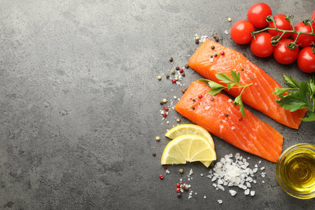 Seafood. Pieces of salmon fillet, tomatoes, lemon slices, oil and spices on gray textured table, flat lay. Space for textの写真素材