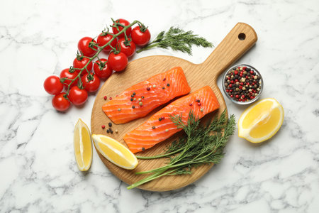 Seafood. Pieces of salmon fillet, spices, tomatoes and lemon wedges on white marble table, flat layの写真素材