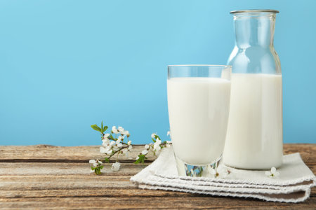 Fresh milk and blossoms on wooden table against light blue background, closeup. Space for textの写真素材