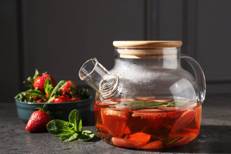 Glass teapot with aromatic fruit tea, strawberries and mint on gray table, closeupの写真素材