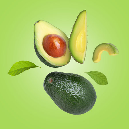 Fresh avocado fruits and leaves falling on light green backgroundの写真素材