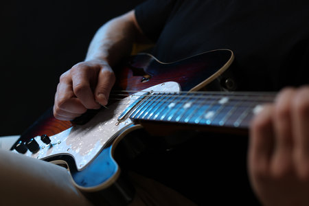 Man playing guitar with mediator on black background, focus on handの写真素材