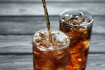 Pouring refreshing cola into glass at gray wooden table, closeup