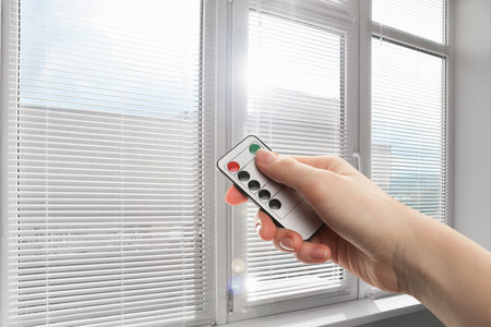 Woman using remote to control blinds in room, closeupの写真素材