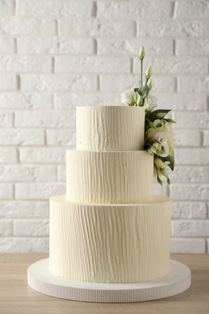 Delicious wedding cake decorated with flowers on wooden table near white brick wallの写真素材